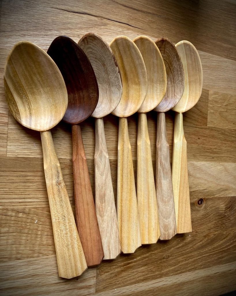 Hand-carved-wooden-spoons-in-varying-hues-arranged-in-a-row-slightly-overlapping-each-other.