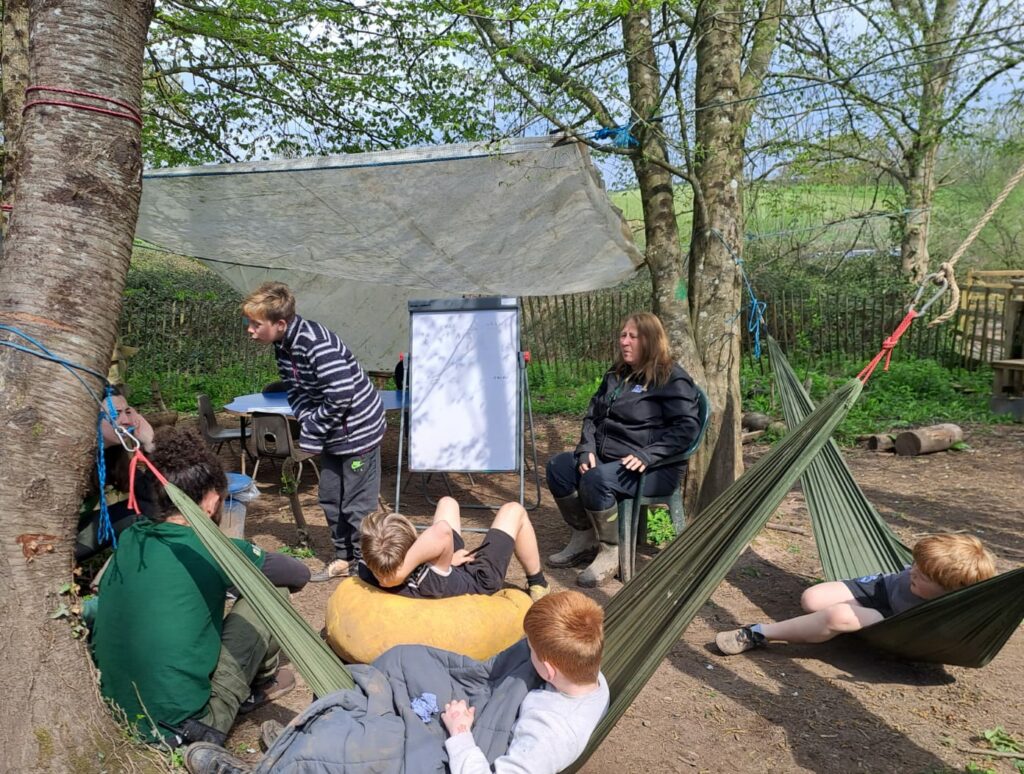 group of children learning outdoors in the woods in hammocks and on bean bags