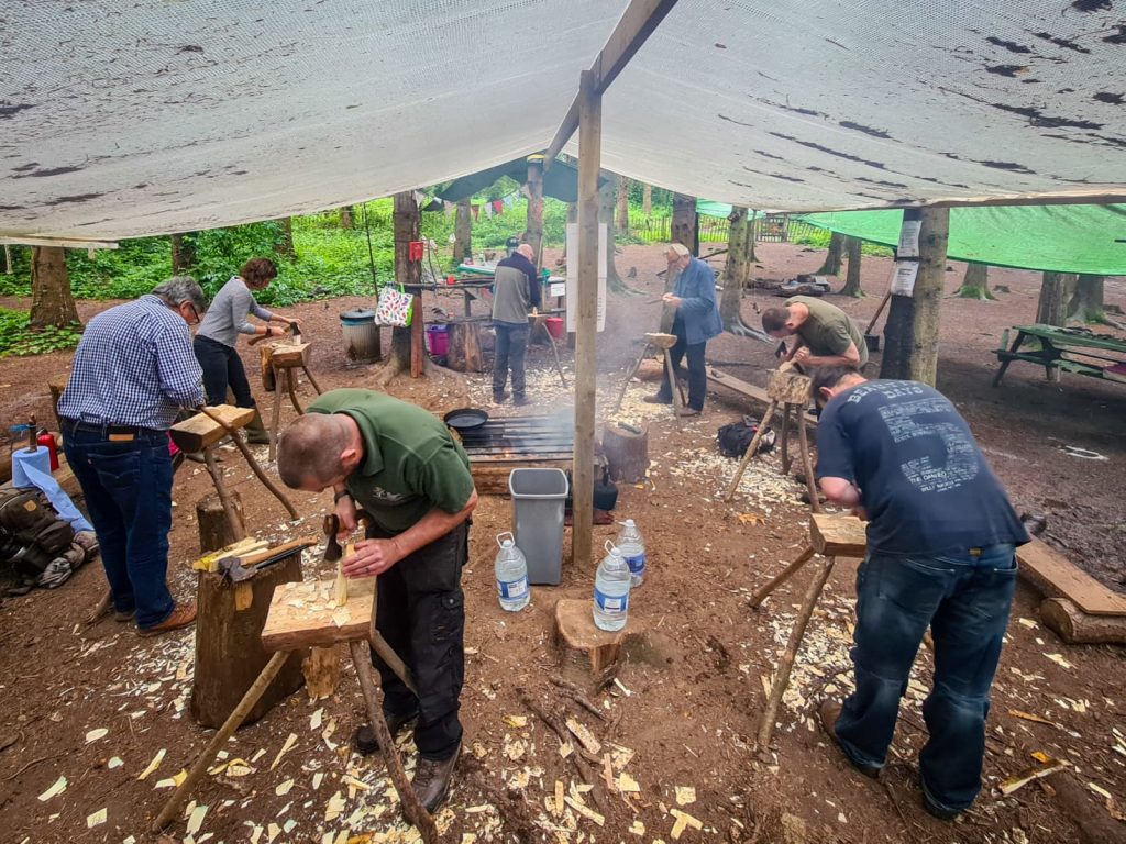 Group of people carving spoons outdoors at a workshop in the woods