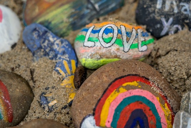 Brightly-painted-stones-nestled-on-a-beach. One-with-the-word-love-and-one-with-a-rainbow-are-prominent.